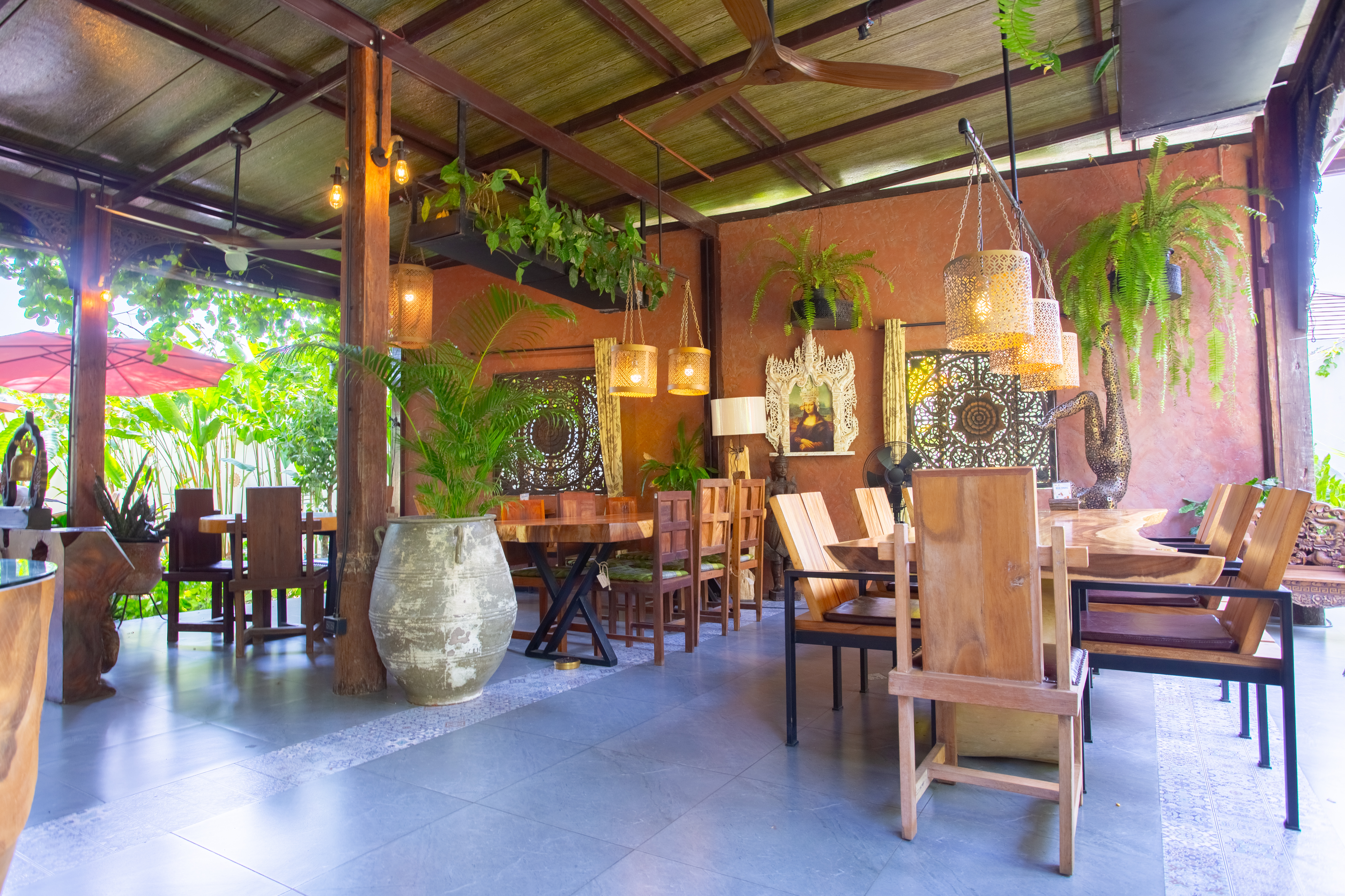 Wooden tables and chairs beneath hanging lights and greenery