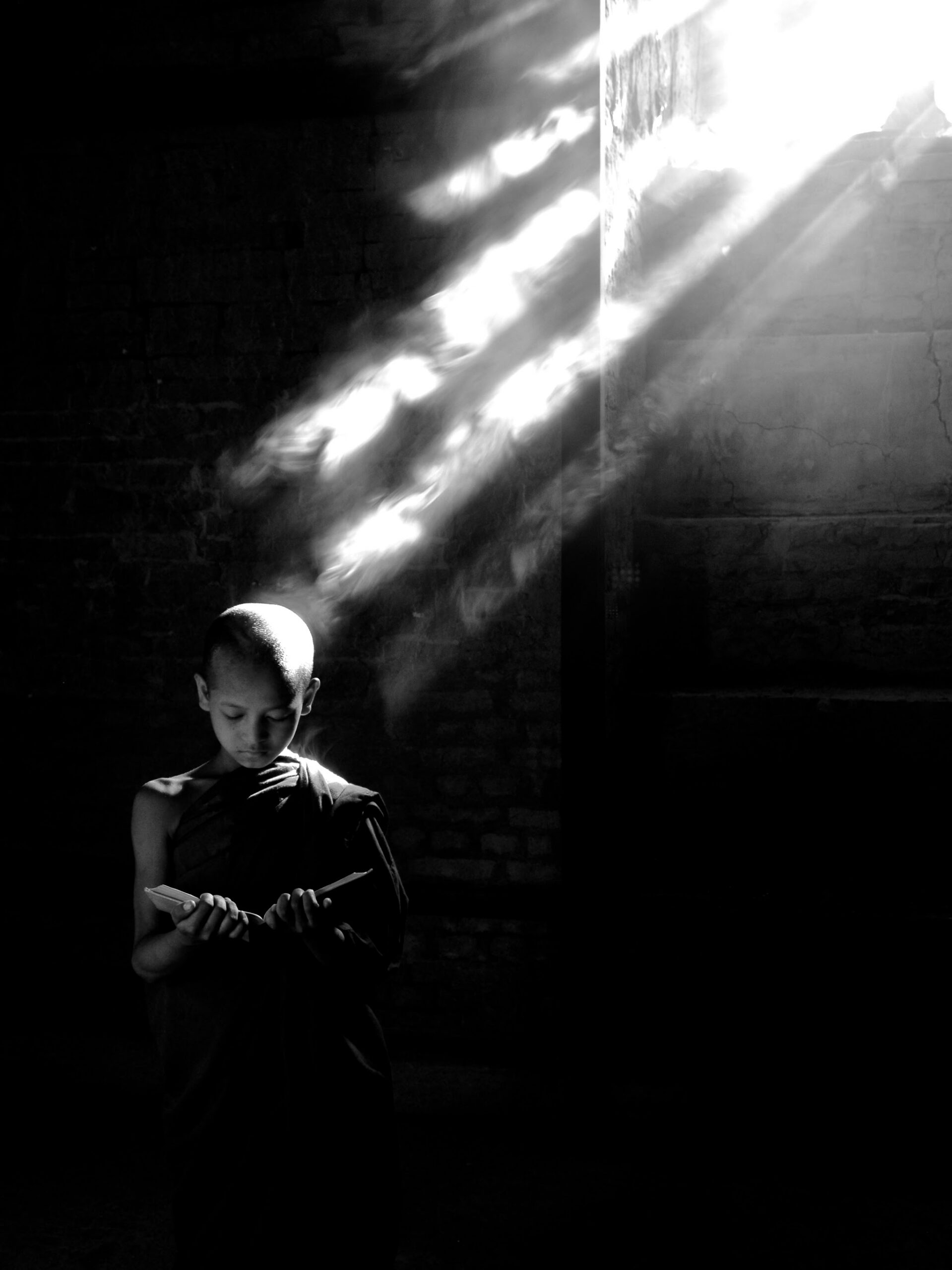Young monk standing beneath beams of light